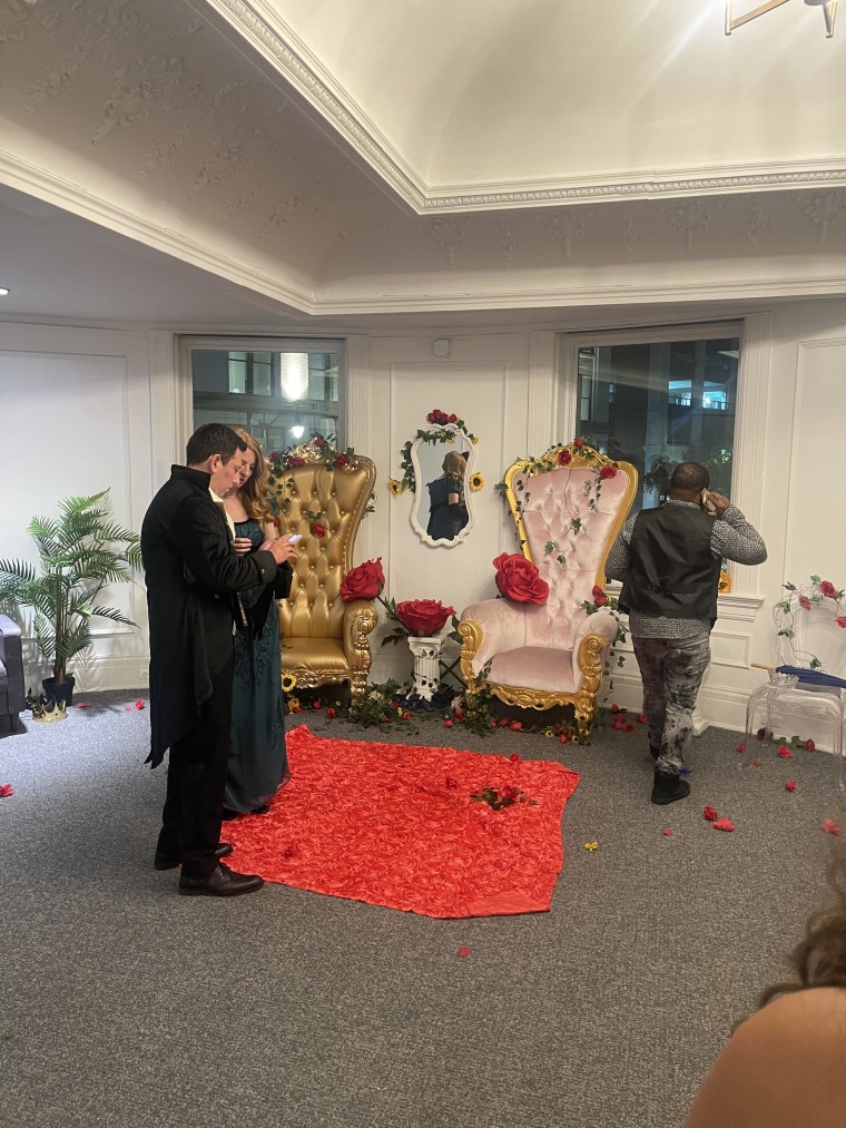 A gold and pink chair with red fake roses on them and a red rug.