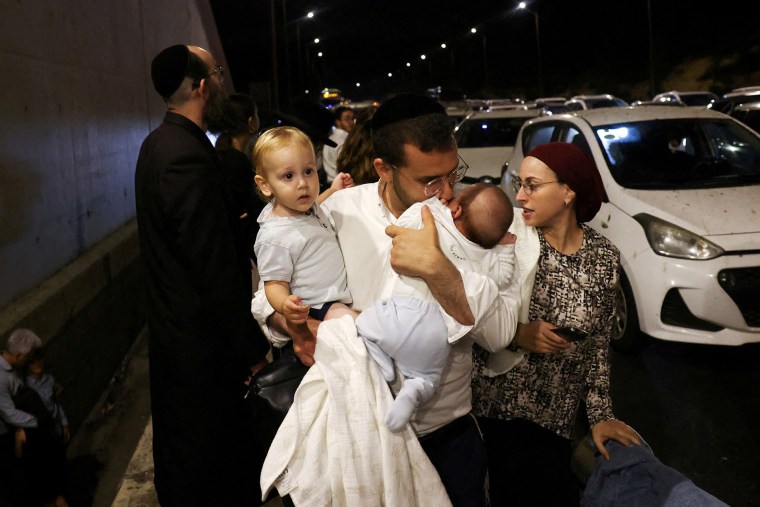 A man holds children as people take cover during an air raid siren, in central Israel