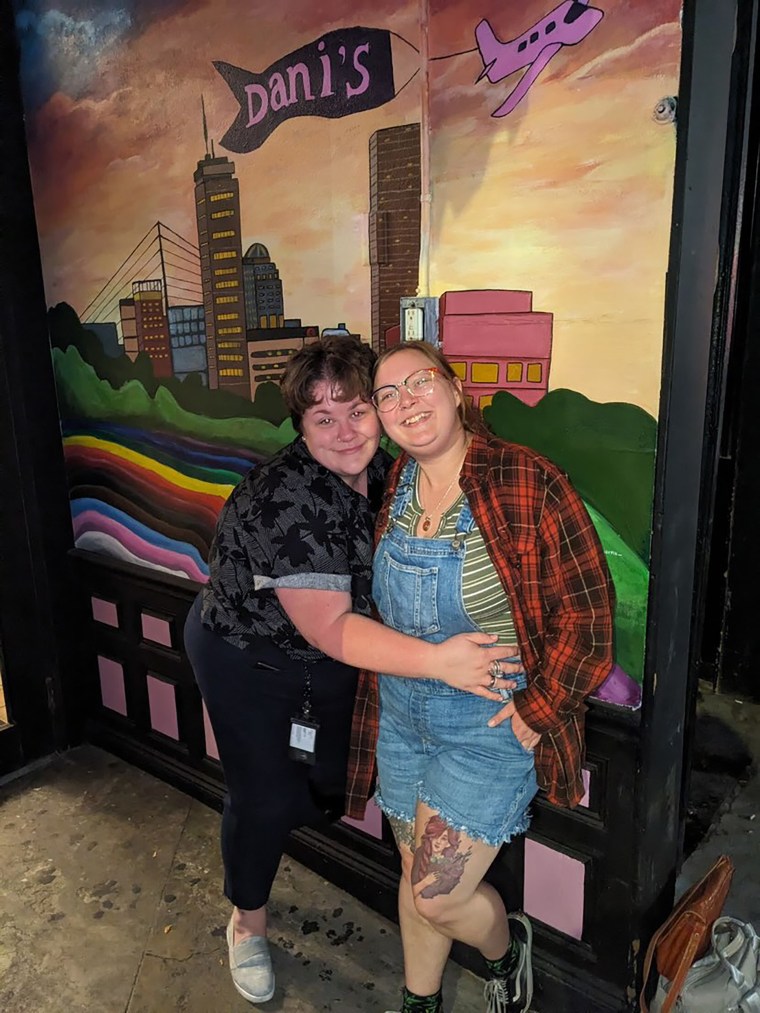 Stevie Dickie e sua namorada, Jace Williams, posam em frente a um mural do lado de fora do Dani's Queer Bar. 