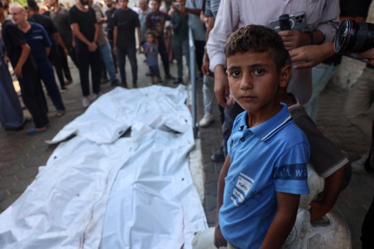 A boy stands near the bodies of people killed in a house hit by an Israeli strike 