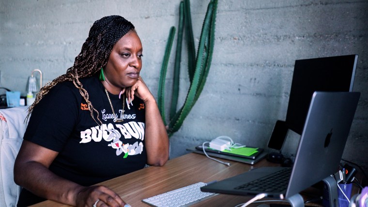 Jasmine Ellis is sitting at a desk in the office using her laptop