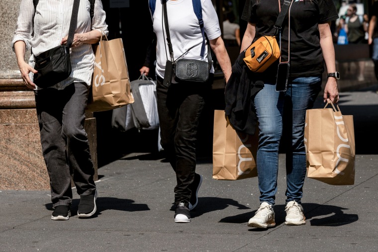 Compradores carregam sacolas da Macy's enquanto caminham na calçada