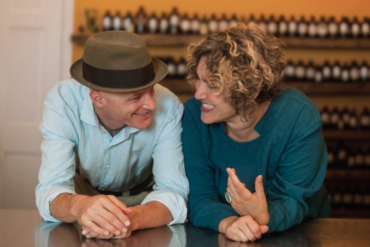 Andrew Selwyn and Maia Toll talk to each other behind a counter inside of a shop