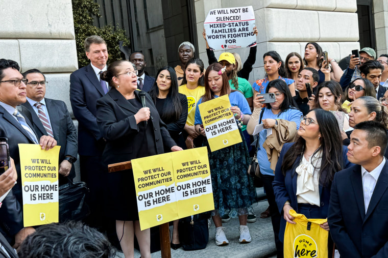 Nina Perales speaks at a podium outside of the United States Fifth Circuit Court of Appeals building, with protestors around her