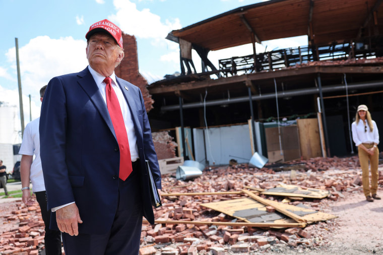 Donald Trump looks around at a building filled with rubble and a street outside