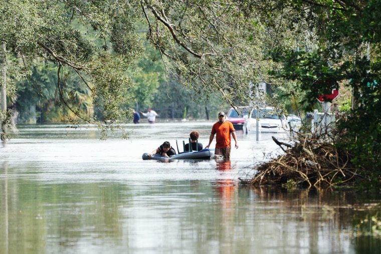 A resident tows an air mattress with people on it through flooded streets in Tampa, Fla., on Oct. 10, 2024.