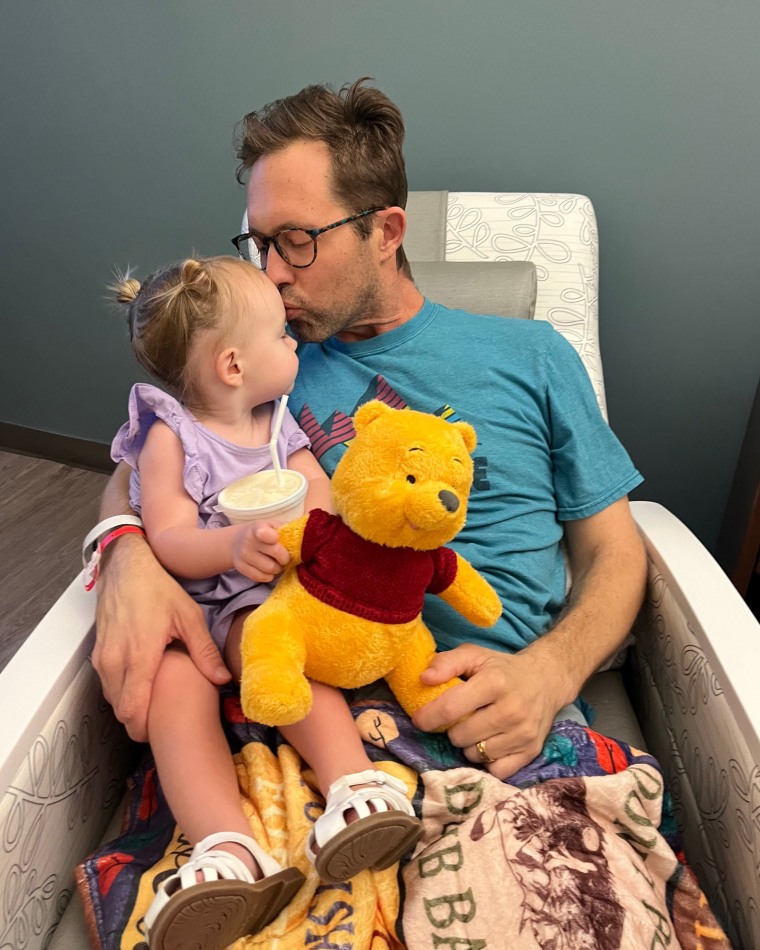 Michael Warren kisses his daughter, seated in his lap, on the forehead, as she holds a Winnie the Pooh stuffed animal