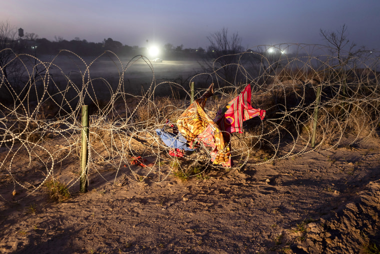 Discarded blankets and clothing hang caught in razor wire outside at night