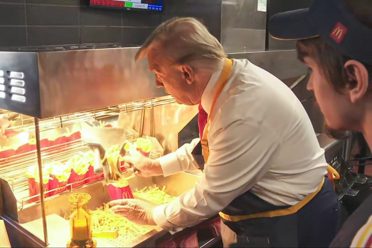 Donald Trump stands in a McDonald's kitchen, wearing an apron and loading up fries