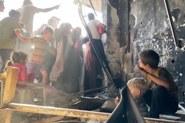 As crowds surge for bread in Gaza, a boy helps his younger brother to drink