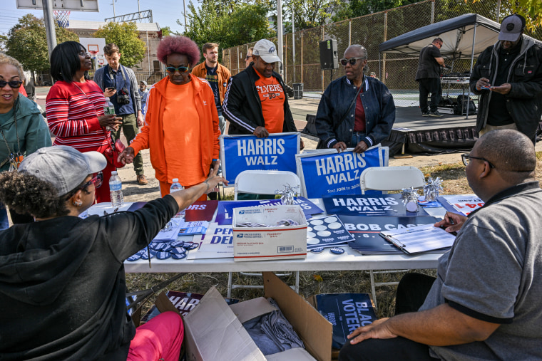 Harris/Walz campaign volunteers hand out campaign posters.