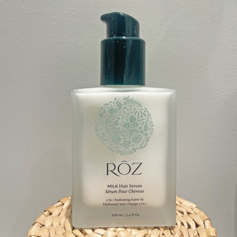 A bottle of Roz Milk Hair Serum sits on top of a wooden coaster.