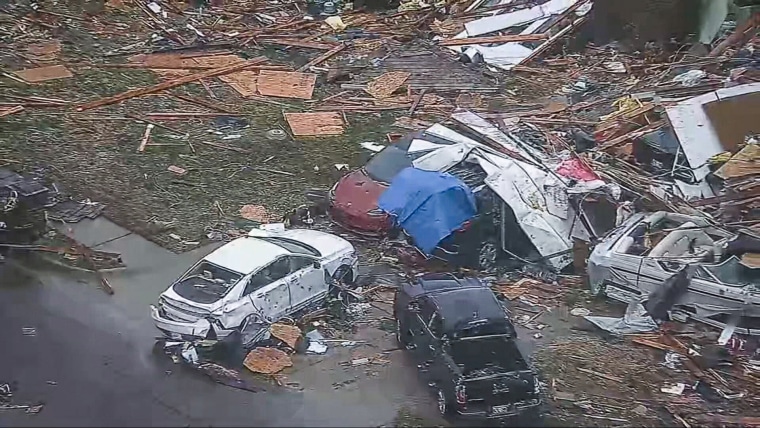 An aerial view of damaged cars surrounded by debris on the road and a lawn