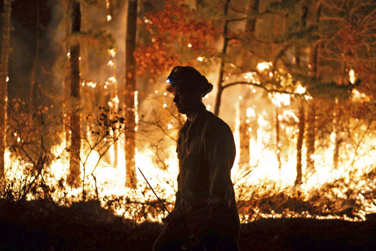 A firefighter is silhouetted against a forest fire on Wednesday, Nov. 6, 2024 in Evesham, N.J.   