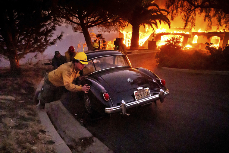 Firefighters and sheriff's deputies push a vintage car away from a burning home