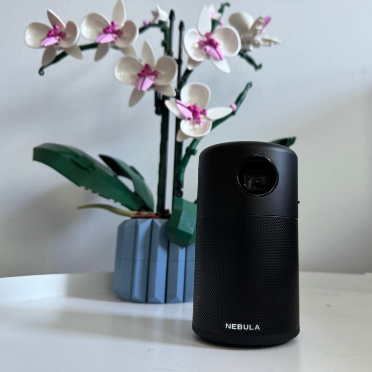 The Anker Nebula Capsule on a white table, beside a Lego Orchid plant.