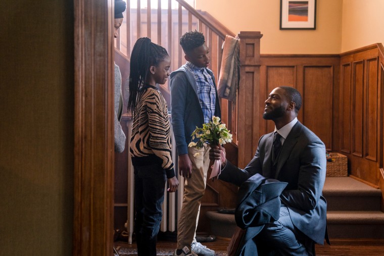 From left, Melody Hurd as Janelle Hodge, Caleb Elijah as Damon Hodge, and Aldis Hodge stand by a stairwell, and Aldis holds flowers while kneeling