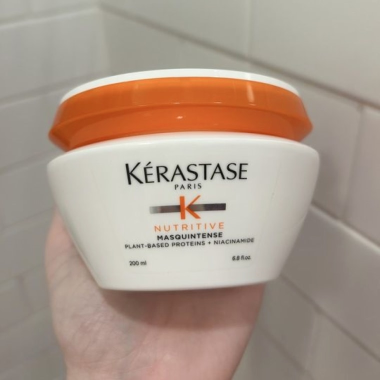 Woman holds Kérastase Nutritive Masquintence Hair Mask in her hand.