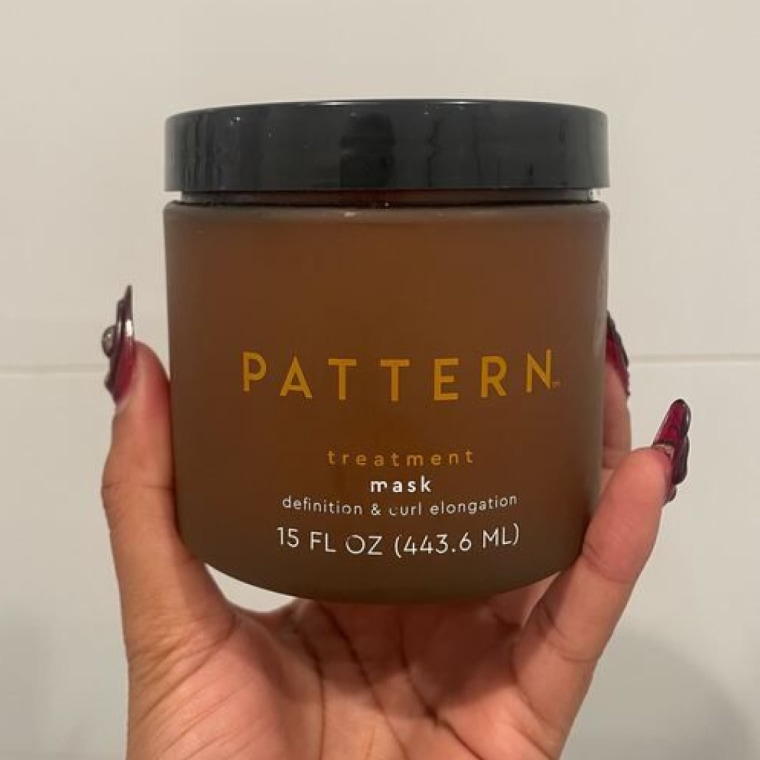 Woman holds up the Pattern Treatment Hair Mask in her hand against a wall.