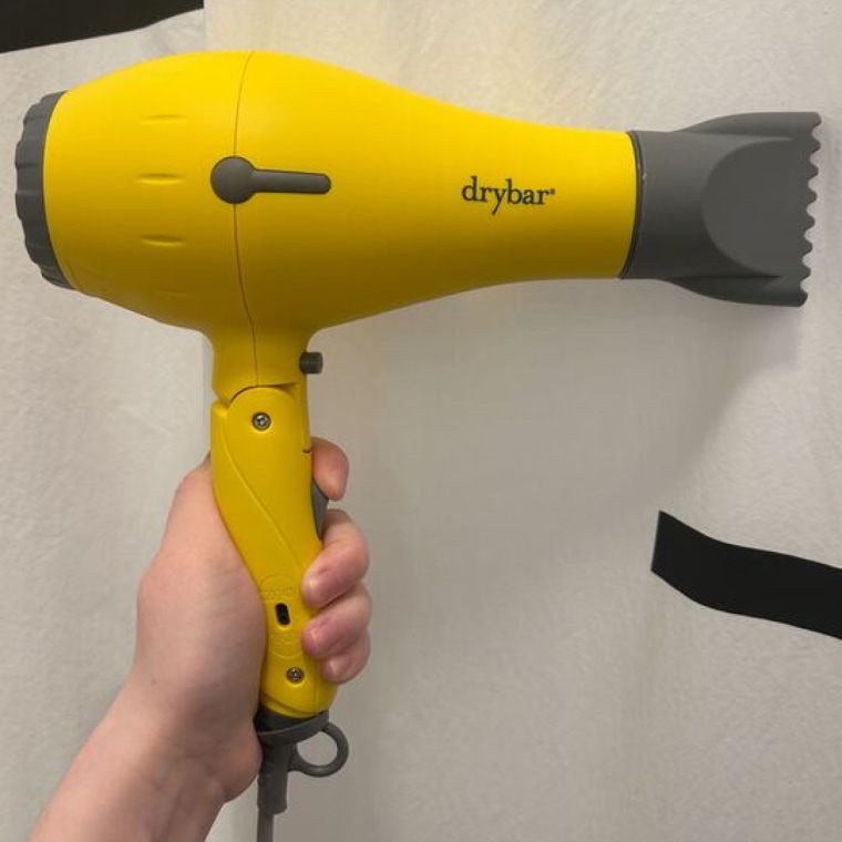 A woman holds an unfolded Drybar Baby Buttercup Travel Blow-Dryer in her hand.