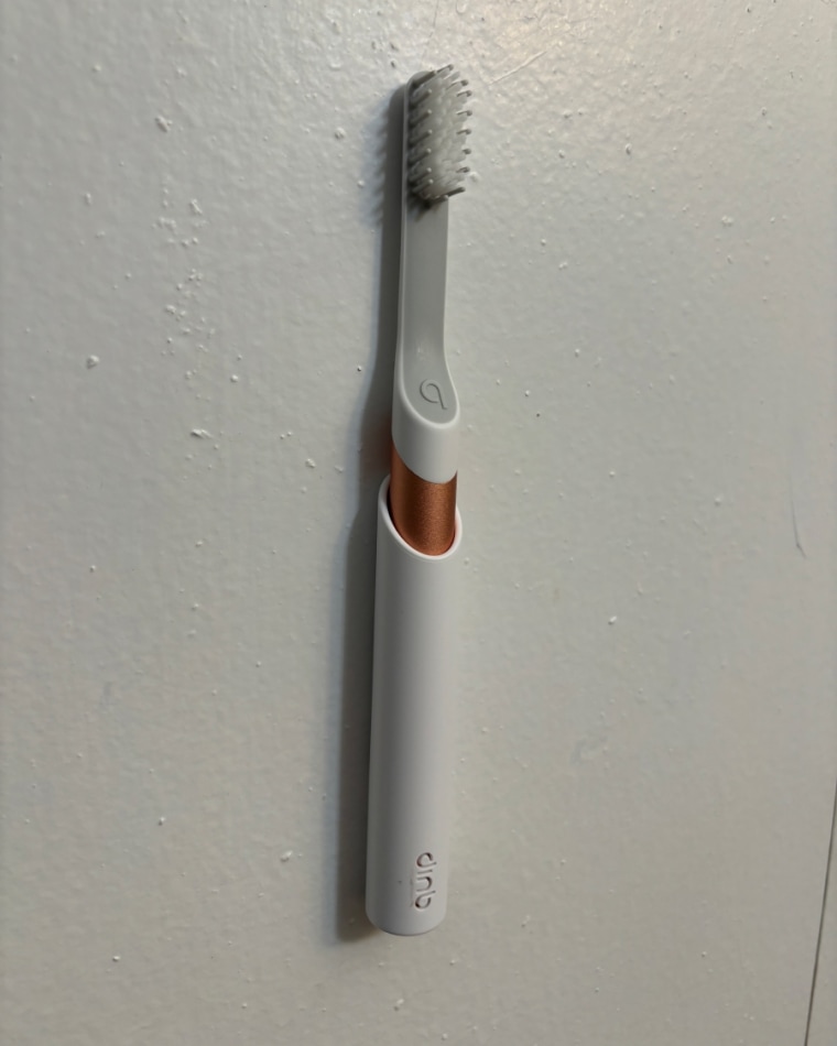 A Quip Electric Toothbrush standing up in its white holder that’s attached to a white wall.