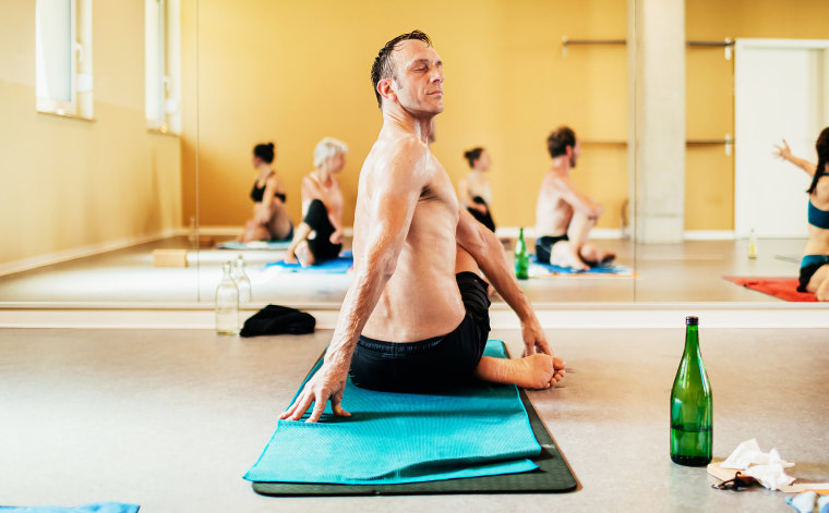 A man sitting on his towel and twisting backwards while performing a pose in a hot yoga class.