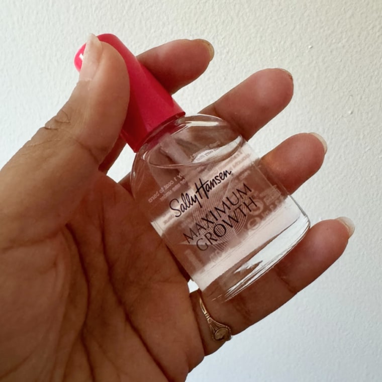 A left hand holding the Sally Hansen Maximum Growth strengthener in front of a white wall.