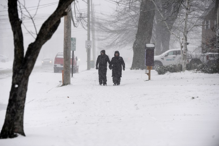 A couple makes their way through snow on a sidewalk