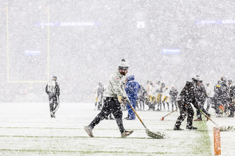 Grounds crew members shovels snow off the yard lines on a football field