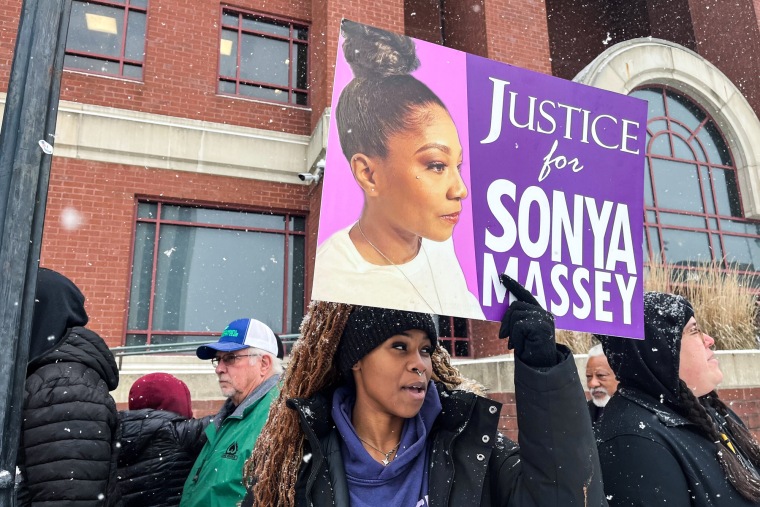 A woman holds a sign that reads "Justice for Sonya Massey"