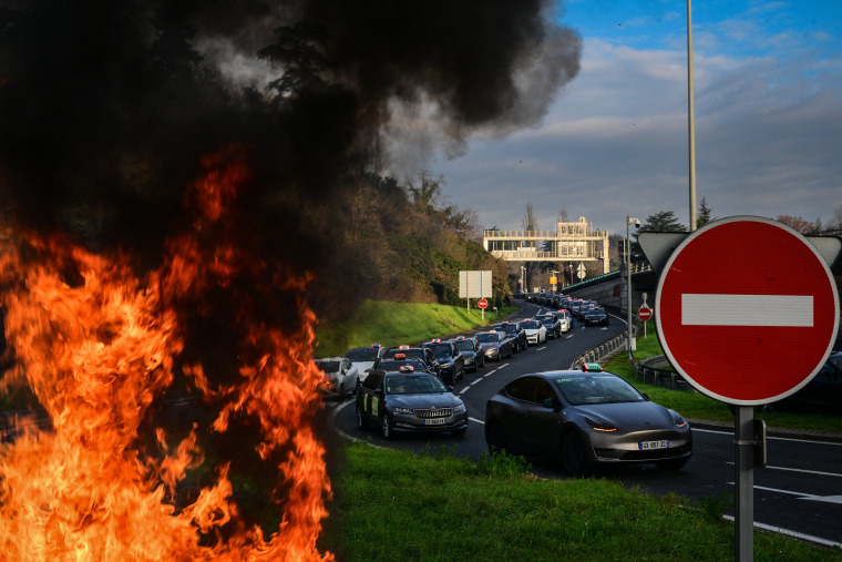 Um incêndio é visto enquanto motoristas de táxi bloqueiam as estradas durante uma manifestação contra um novo sistema de preços decrescentes para transporte médico e uma 