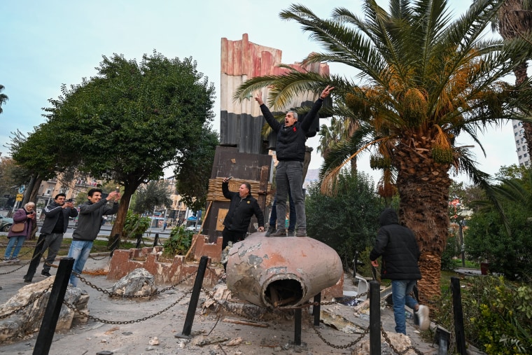 People stand atop a toppled statue of Syria's late president Hafez al-Assad in Damascus