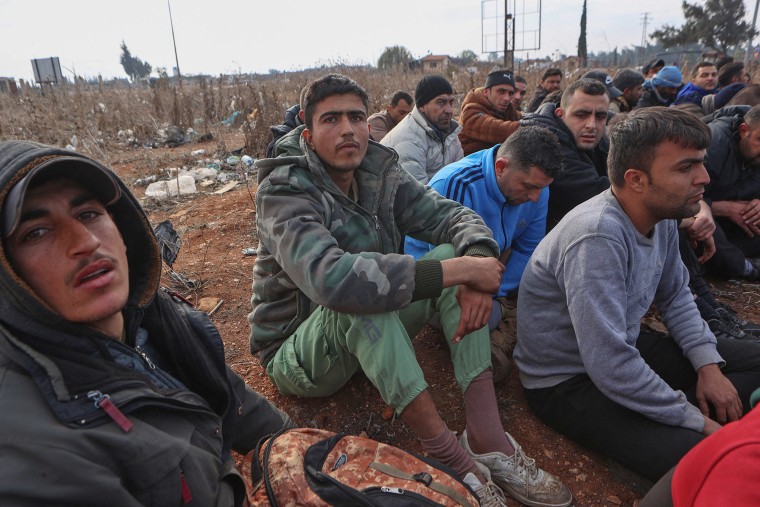 Detained members of the Syrian government security forces are gathered outdoors at a makeshift detention facility