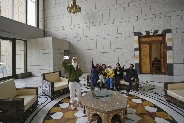 A group poses for a photo while sitting on a couch in a hall of Syrian President Bashar Assad's presidential palace in Damascus, Syria, Sunday, Dec. 8, 2024. 