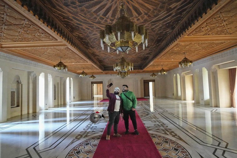 Two men pose for a selfie while walking through the halls of Syrian President Bashar Assad's presidential palace in Damascus, Syria, Sunday, Dec. 8, 2024. 