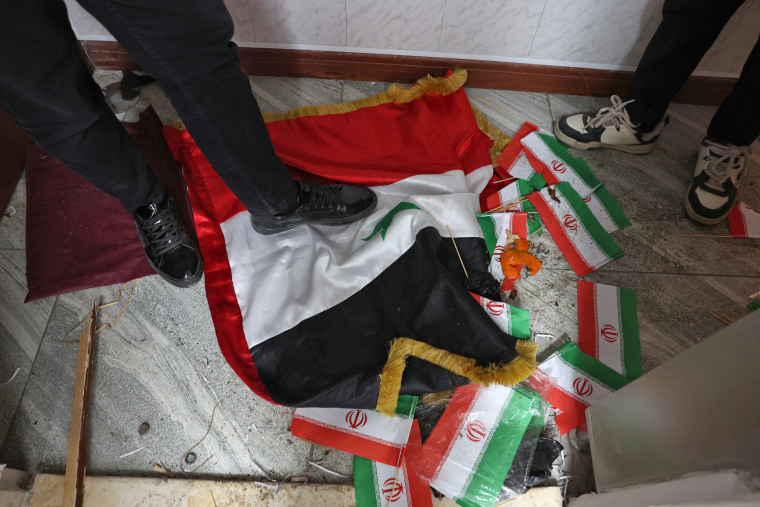 A man steps on a Syrian regime flag next to Iranian national flags in a ransacked office at Iranian embassy in the capital Damascus on December 8, 2024.