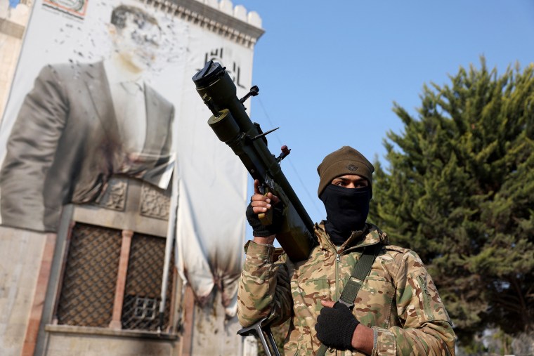 An anti-government fighter stands in front of a defaced portrait of Syrian President Bashar al-Assad in Hama after forces captured the central Syrian city on Dec. 6, 2024. 