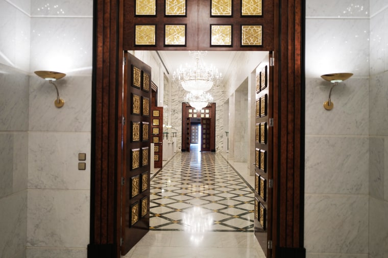 A hallway lined with marble and ornate chandeliers. 