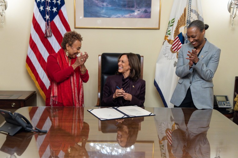 Kamala Harris sits between two standing women as she signs an act into law