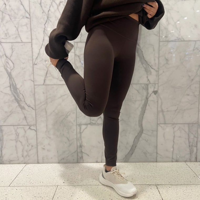 Woman stretches wearing brown Alo ⅞ High-Waist Airlift leggings.