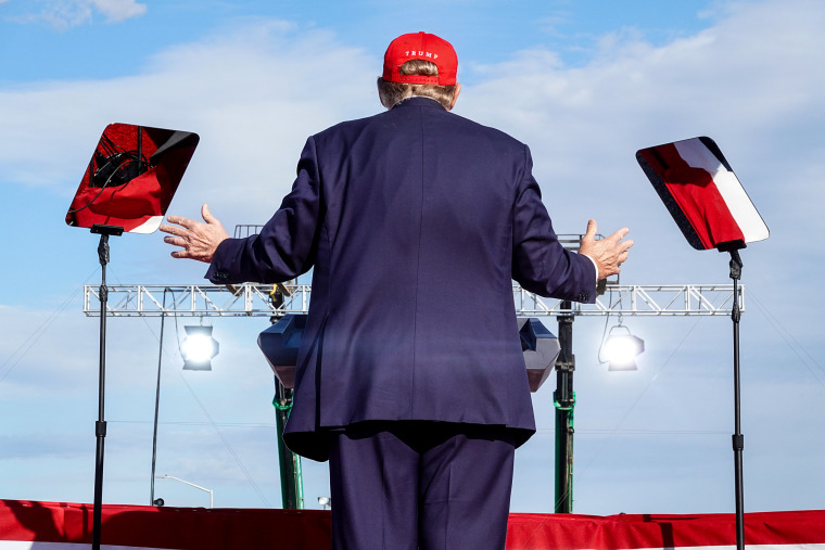 Donald Trump, back to camera, speaks at a podium outside