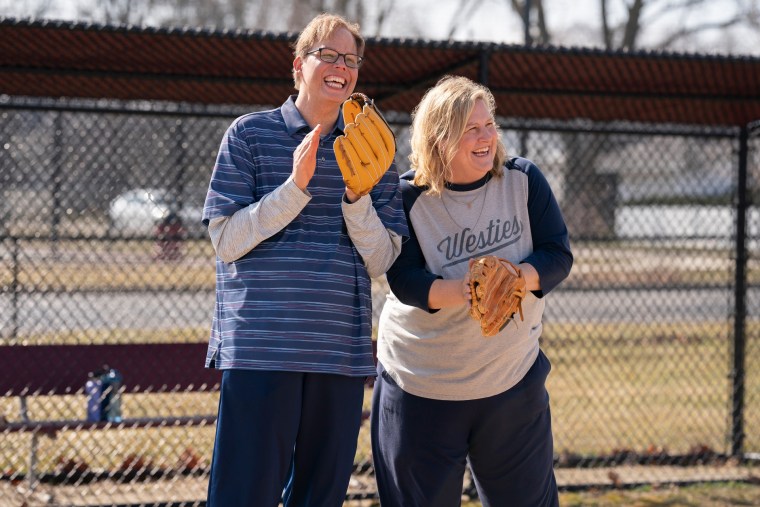 Jeff Hiller y Bridget Everett están afuera en el campo de béisbol con sus guantes de béisbol.