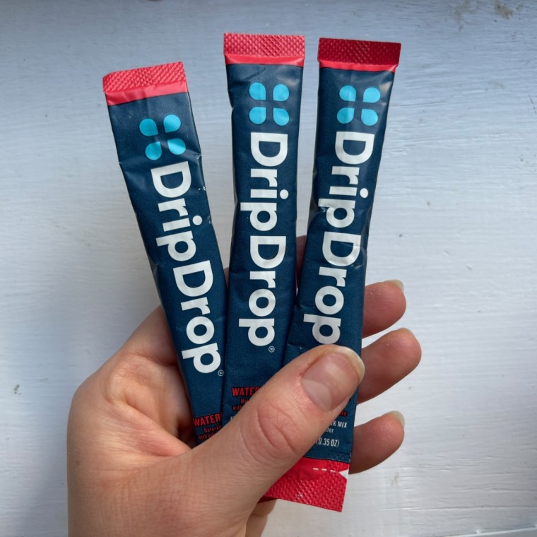 A hand holding three single-serve packets of DripDrop’s electrolyte powder.