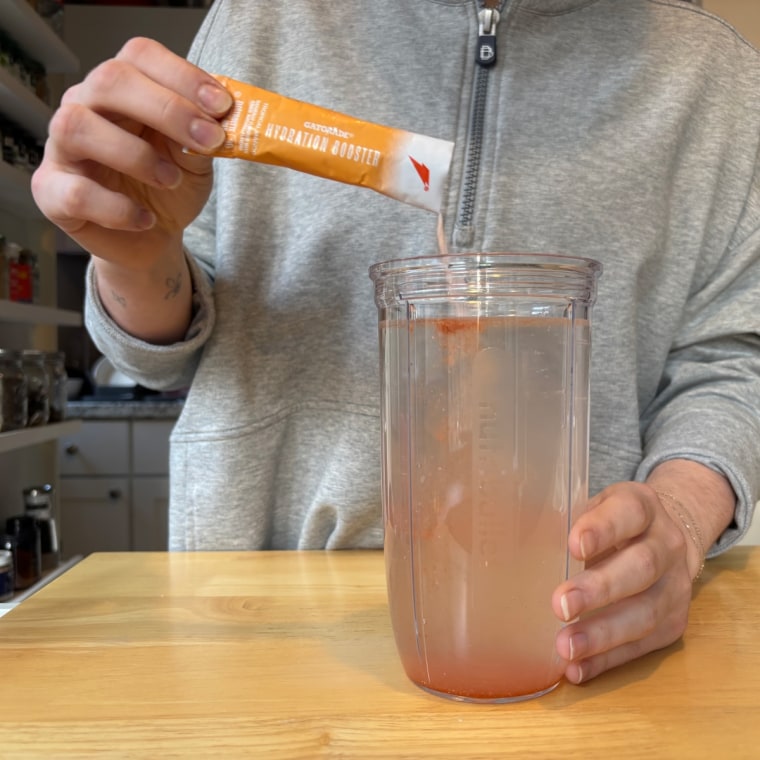 A person pouring a single-serve packet of Gatorade electrolyte powder into a cup of water.