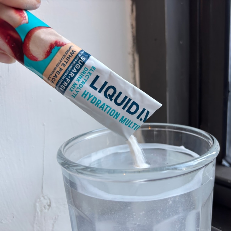 A hand pouring a single-serve packet of Liquid I.V. electrolyte powder into a glass of water.