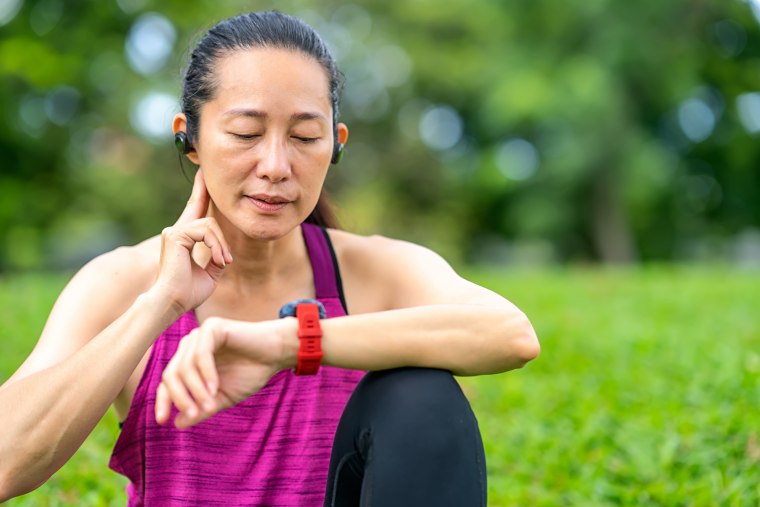 Asian women take their pulse and read data on a smartwatch after running outdoors at a public park. 