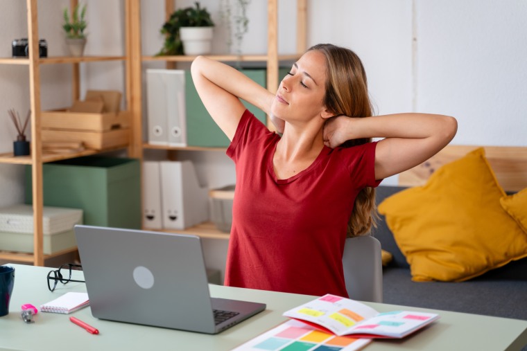 Young woman taking a break from work, stretching her neck in a cozy office environment