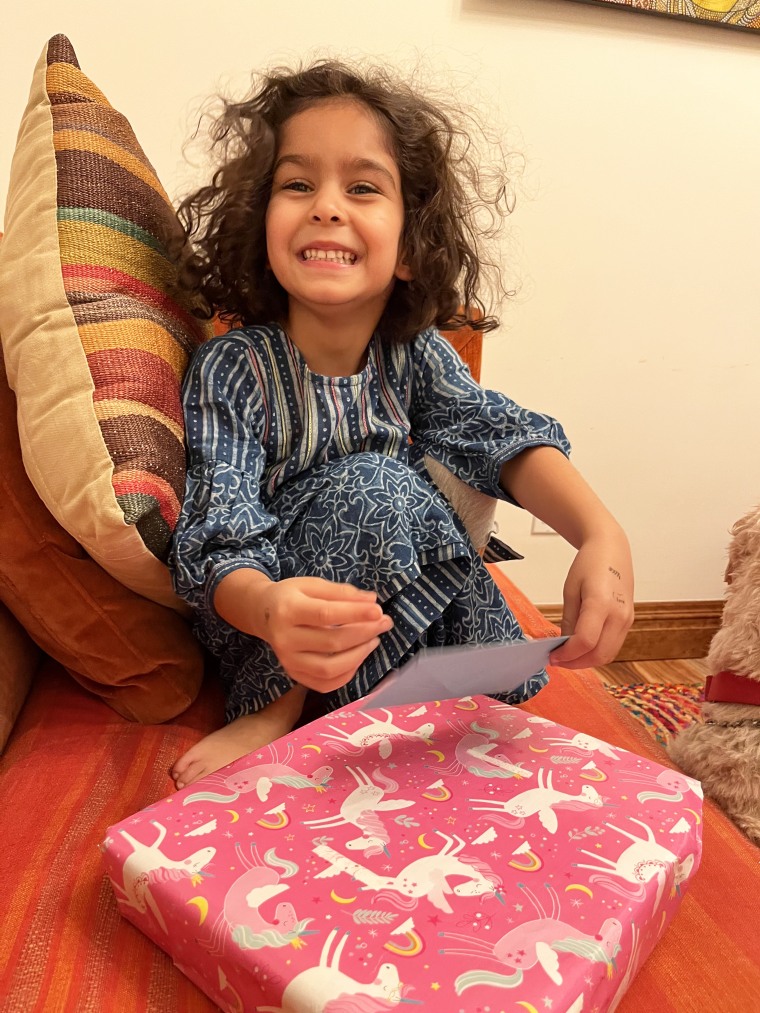 Young girl sits on a couch, opening a birthday present.