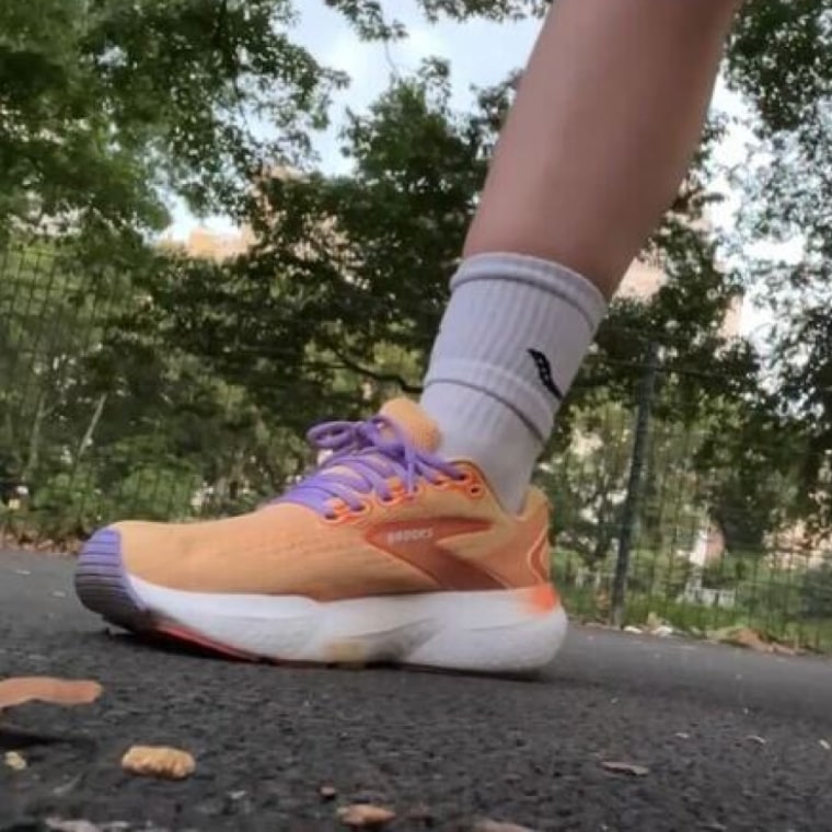 Woman wears orange Saucony sneakers and white crew-length Saucony socks.