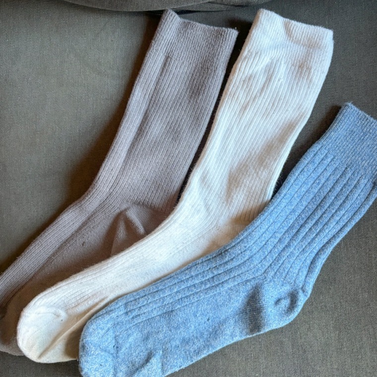 Gray, light blue and white socks laid on a couch next to one another.